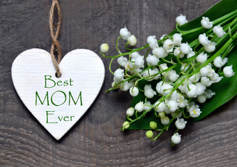 Best Mom Ever.Bouquet of lilies of the valley and decorative heart with greeting text on wooden background.Lily-of-the-valley flowers. Mother's Day festive concept.Selective focus.