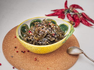 Vegetarian light salad with seaweed and sesame in a ceramic decorative salad bowl stands on a cork stand.