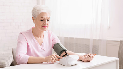 Senior woman measuring her blood pressure at home.