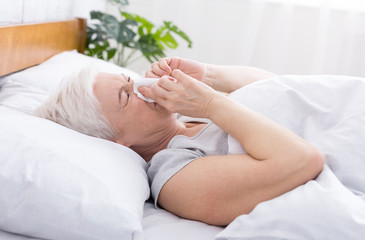 Fototapeta na wymiar Senior woman covering nose with tissue while sneezing at home