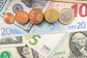 row of coins on background of various Euro and Dollar banknotes