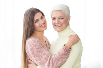 Senior mother and daughter embracing and looking at camera