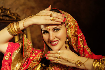 Portrait smiling of beautiful indian girl at home. Young woman model with golden jewelry set .