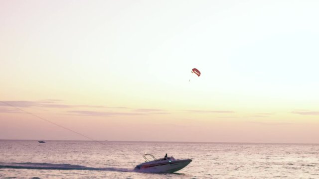 Parachute activity0 at tropical beach after sunset, shot of boat towing parachute with people. Calm sea waters and beautiful neat sky on background