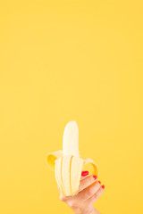 Healthy nutrition. Hand holding half peeled banana. Copy space on yellow background.
