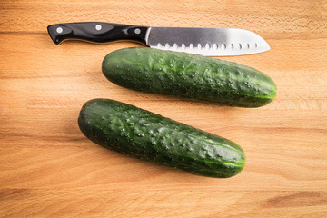 two whole green cucumbers next to a knife