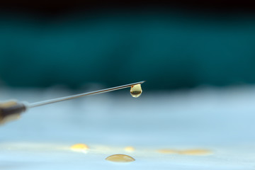 A drop of medicine hangs on a needle point of a syringe against a dark background.