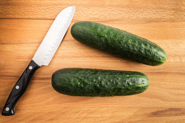 two whole green cucumbers next to a knife