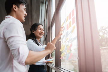 asian male and female business partner brainstorming by sticking idea into the glass window