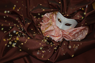 Weiße Karnevlasmaske auf braunem seidentuch mit goldenem Konfetti und Pailetten