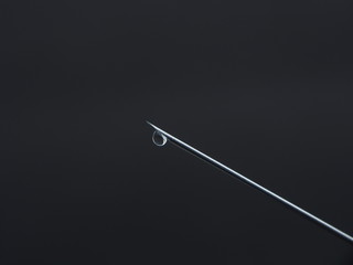 A drop of medicine on the end of a medical syringe needle.