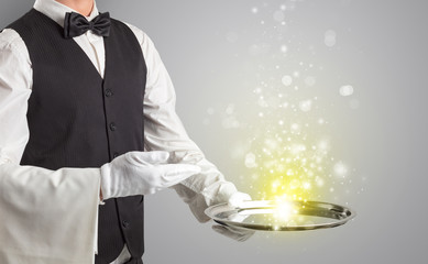 Elegant young waiter serving mysterious light on tray
