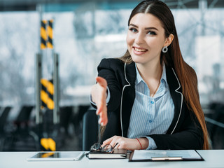Friendly HR portrait. Smiling intern woman standing at counter extend welcoming hand. Office workspace.