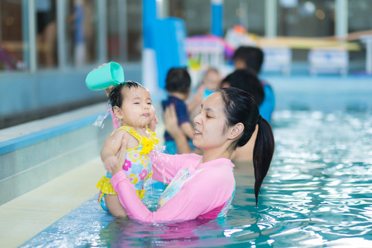 Mother Pouring Water On Baby Head  To Teach Her Baby. Early Development Class For Infants Swimming. Baby Swimming Concept. Mother And Baby Swim In The Pool.