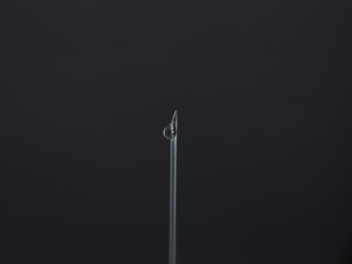 A drop of medicine on the end of a medical syringe needle.