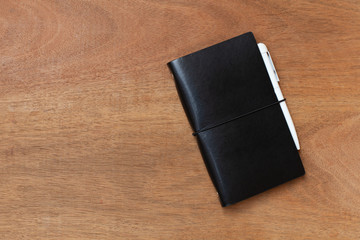 Black leather diary and pen on wooden background. Top view and Copy space