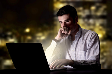 Young handsome businessman working late at night in the office with city lights in the background