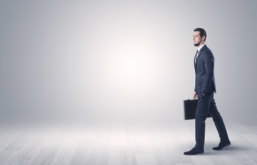 Obraz premium Successful businessman walking in front of an empty wall with briefcase on his hand 