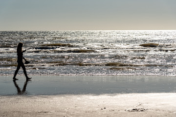 Fototapeta na wymiar Woman silhouette walking on the shore using her cell phone