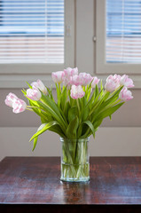 A fresh and clean home office with soft pink tulip flowers on a dark wooden table for Valentine's Day celebration. Airy Scandinavian/Nordic interior style on a media office in Finland.