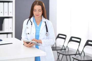 Doctor woman at work. Portrait of female physician using digital tablet  while standing near reception desk at clinic or emergency hospital. Medicine and healthcare concept