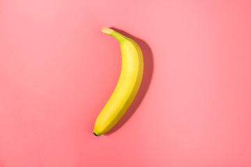 Single banana on a pink background with strong shadow
