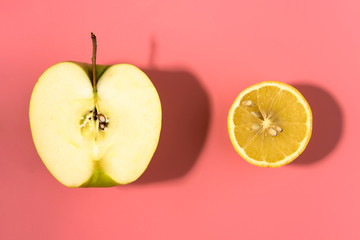 Sliced lemon and green apple on pink background with contrast shadows