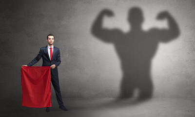 Businessman standing with red cloth on his hand and strong hero shadow on the background
