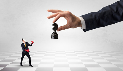 Small businessman fighting against big chessman on a big hand with chess board concept
