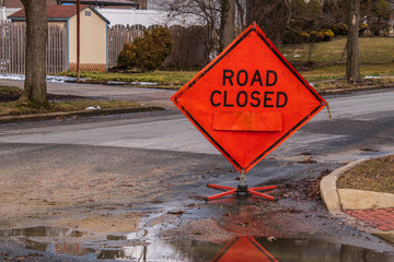 Orange diamond shaped road closure sign on road in a neighborhood near a house.