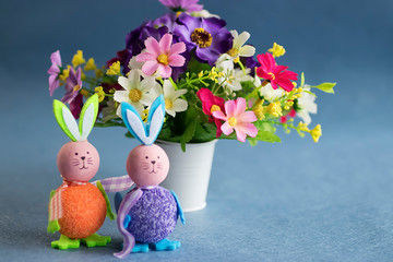 Two decorative rabbits and bright flowers on a gray background. Easter concept.