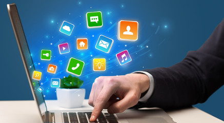 Businessman hand typing on laptop with flying application icons around
