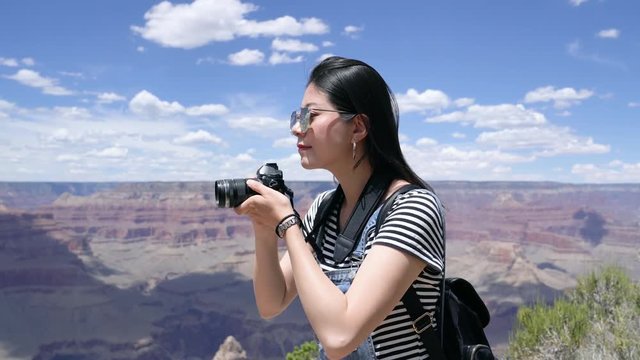 asian woman in sunglasses taking amazing nature wild picture by slr camera smiling satisfied with beautiful desert view. toursit visiting Grand Canyon National Park. young girl backpacker enjoy happy