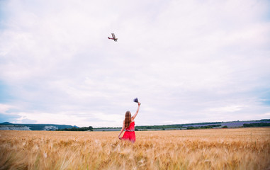 The girl in the red dress at wheat field waving at the plane