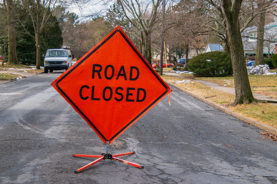 Orange diamond shaped road closure sign on road in a neighborhood near a house.