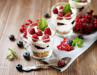 Healthy breakfast - yogurt with fresh  berries and muesli served in glass jar, on wooden background