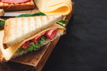 Sandwiches on a cooking board, grilled toast, salami sausage, salad lettuce and cheese on a dark background