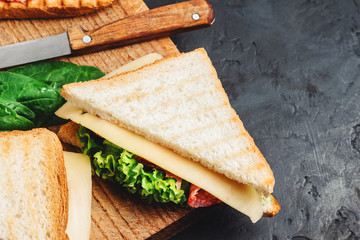 Sandwiches on a cooking board, grilled toast, salami sausage, salad lettuce and cheese on a dark background