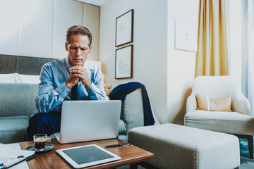 Serious adult man frowning while sitting in front of the laptop