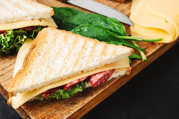 Sandwiches on a cooking board, grilled toast, salami sausage, salad lettuce and cheese on a dark background