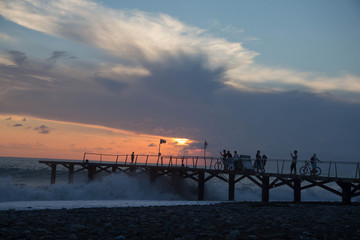 sun setting over Batumi beach Jetty, as powerful waves roll in, and a very colorful sky is reflected on the beach