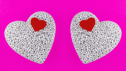 Small red wooden heart lying on a large white stone heart with pores. Pink background. View from above. Mirroring.