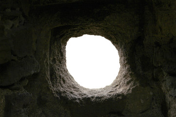 round uneven hole in dark stone wall with white background. loophole in the fortress wall