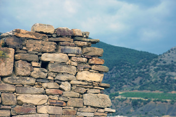 old ancient ruined stonework wall of bricks and stone blocks foreground closeup green mountains background