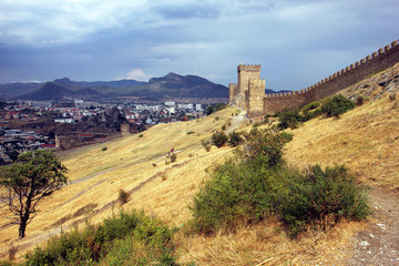 Fototapeta na wymiar landscape with a stone fortress wall on a hill with yellow scorched grass on the background of mountains and sky