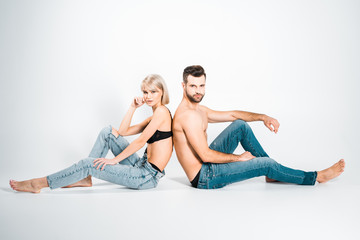 beautiful girlfriend and handsome boyfriend in underwear and jeans sitting back to back on grey