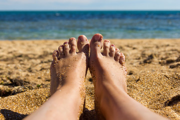 view of the feet of a sunbathing girl on the beach by the sea