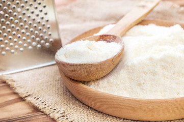Wooden bowl and wooden spoon with grated parmesan and grater on wooden background. Top view. Space for text.