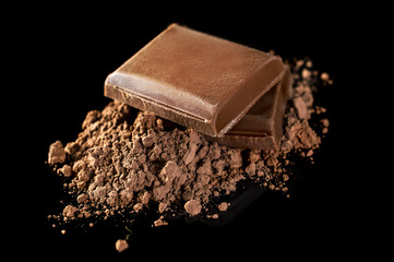 Piece of chocolate bar with heap of cocoa powder on black.