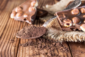 Pieces of chocolate bar with nuts, cocoa powder and sack napkin on the table.